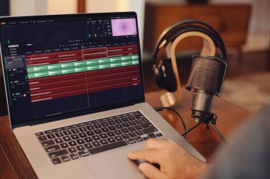 Hands on laptop computer with audio editing software with microphone and headphones in background
