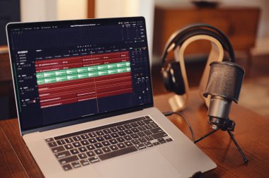 Laptop computer with audio editing software with microphone and headphones in background