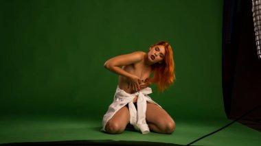 Stüdyoda yeşil arka planda beyaz gömlekli çıplak kızıl kadın. 