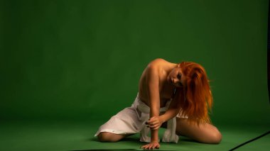 Stüdyoda yeşil arka planda beyaz gömlekli çıplak kızıl kadın. 