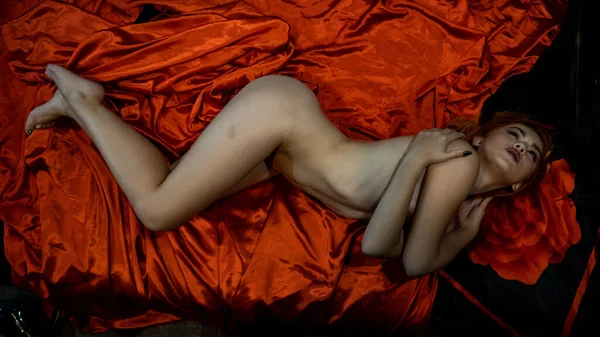 Stüdyoda kırmızı ipekli çıplak kadın poz veriyor. 
