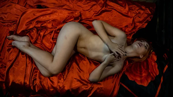 Stüdyoda kırmızı ipekli çıplak kadın poz veriyor. 