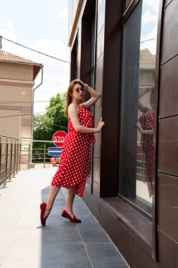 Şehir caddesinde poz veren yaz kırmızı elbiseli çekici genç bir kadın. 