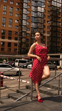 Şehir caddesinde poz veren yaz kırmızı elbiseli çekici genç bir kadın. 