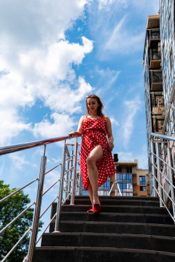 Şehir caddesinde poz veren yaz kırmızı elbiseli çekici genç bir kadın. 