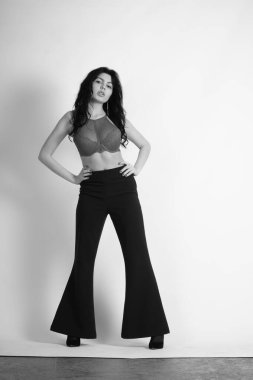 Stüdyoda beyaz arka planda poz veren iç çamaşırlı, esmer, seksi bir kadın. 