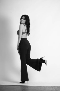 Stüdyoda beyaz arka planda poz veren iç çamaşırlı, esmer, seksi bir kadın. 