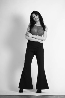 Stüdyoda beyaz arka planda poz veren iç çamaşırlı, esmer, seksi bir kadın. 