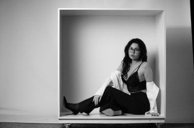 Stüdyoda beyaz arka planda dekoratif bir kutuda poz veren iç çamaşırlı, güzel esmer kadın. 