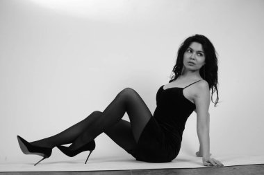 Stüdyoda beyaz arka planda yüksek topuklu giysili, küçük siyah elbiseli seksi esmer kadın. 