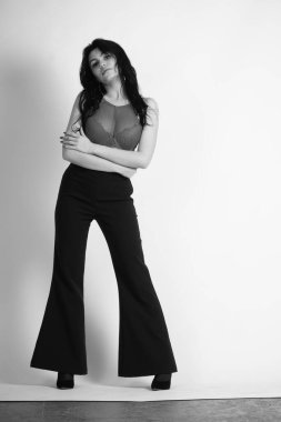 Stüdyoda beyaz arka planda poz veren iç çamaşırlı, esmer, seksi bir kadın. 