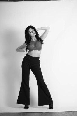 Stüdyoda beyaz arka planda poz veren iç çamaşırlı, esmer, seksi bir kadın. 