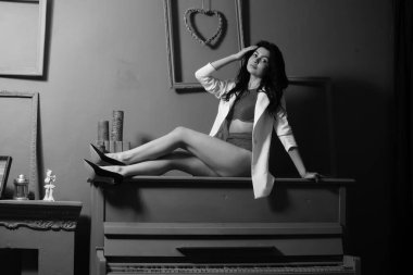 İç çamaşırlı, beyaz ceketli güzel esmer kadın stüdyoda piyanoda poz veriyor. 