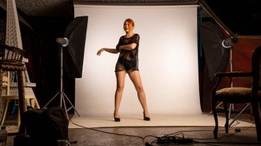 Parlak turuncu makyajlı ve uzun kızıl saçlı çekici bir kız. Stüdyoda beyaz arka planda poz veriyor. 