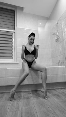 Siyah iç çamaşırlı güzel bir kadın banyoda poz veriyor, siyah beyaz bir fotoğraf.