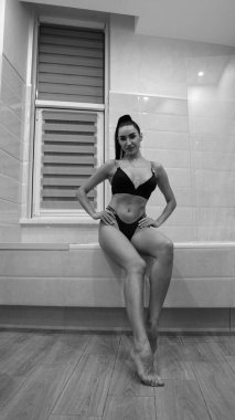 Siyah iç çamaşırlı güzel bir kadın banyoda poz veriyor, siyah beyaz bir fotoğraf.