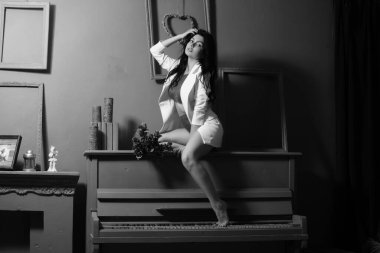 Güzel esmer kadın spor ceketli ve beyaz melek kanatlarıyla stüdyoda piyanonun yanında poz veriyor. 