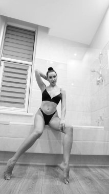 Siyah iç çamaşırlı güzel bir kadın banyoda poz veriyor, siyah beyaz bir fotoğraf.