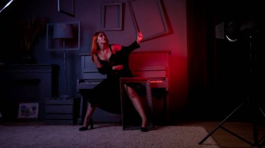 Gece elbisesi içinde piyanoyla poz veren güzel ve çekici bir kadın.