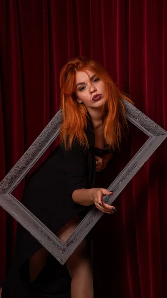 young Red-haired woman posing with empty antique frames on red background