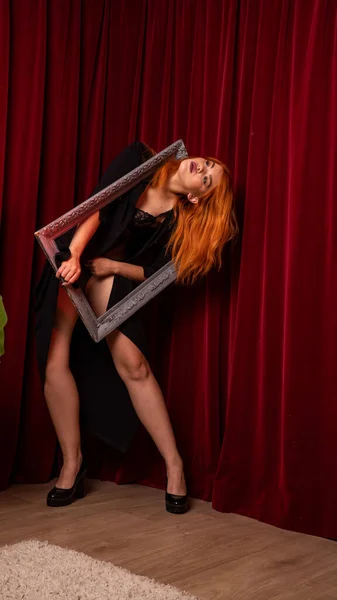 young Red-haired woman posing with empty antique frames on red background