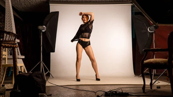 Parlak turuncu makyajlı ve uzun kızıl saçlı çekici bir kız. Stüdyoda beyaz arka planda poz veriyor. 