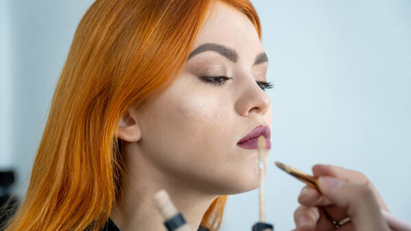 Модель имеют макияж визажиста в салоне красоты. Вид от первого лица. Рыжая модель с веснушками. Закрыть лицо модели макияжем.