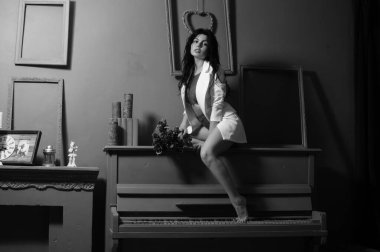 Güzel esmer kadın spor ceketli ve beyaz melek kanatlarıyla stüdyoda piyanonun yanında poz veriyor. 