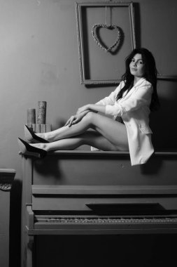 Beyaz ceketli ve iç çamaşırlı güzel esmer kadın stüdyoda piyanoyla poz veriyor. 