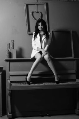 Spor ceketli güzel esmer kadın stüdyoda piyanonun yanında poz veriyor. 