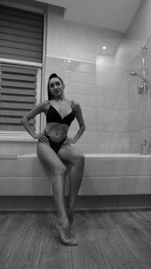 Siyah iç çamaşırlı güzel bir kadın banyoda poz veriyor, siyah beyaz bir fotoğraf.