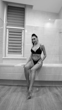 Siyah iç çamaşırlı güzel bir kadın banyoda poz veriyor, siyah beyaz bir fotoğraf.