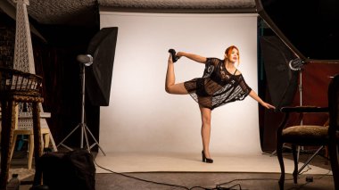 Parlak turuncu makyajlı ve uzun kızıl saçlı çekici bir kız. Stüdyoda beyaz arka planda poz veriyor. 