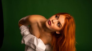 Stüdyoda beyaz gömlek ve külot giyen, yeşil duvar arkasında poz veren çekici, çıplak genç bir kadın.   