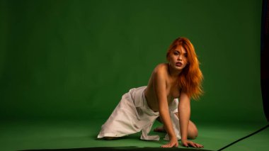 Stüdyoda beyaz gömlek ve külot giyen, yeşil duvar arkasında poz veren çekici, çıplak genç bir kadın.  