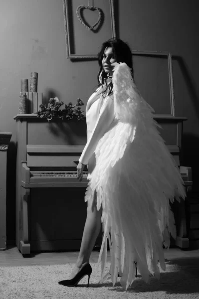 在演播室里 穿着西装的美丽的黑发女人和站在钢琴边的白天使翅膀 — 图库照片