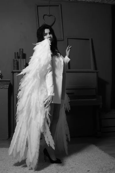 在演播室里 穿着西装的美丽的黑发女人和站在钢琴边的白天使翅膀 — 图库照片