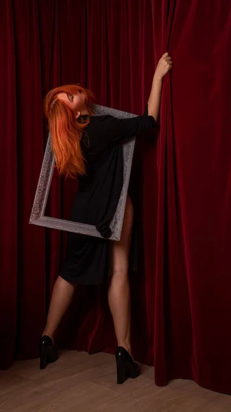 young Red-haired woman posing with empty antique frames on red background