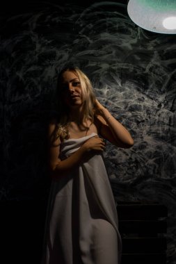 Üstsüz sarışın, siyah arka planda beyaz bir bez ile kaplı.