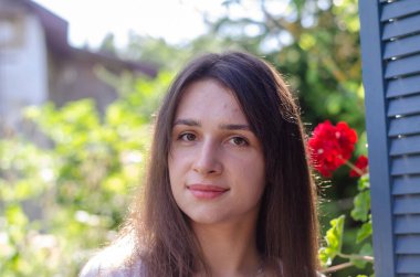 Güneşli bir günde evin yakınındaki yaz bahçesinde poz veren güzel bir genç kız.