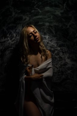 Üstsüz sarışın, siyah arka planda beyaz bir bez ile kaplı.