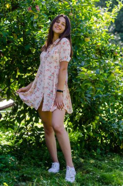 Güneşli bir günde bahçede poz veren yazlık elbiseli güzel bir kız.