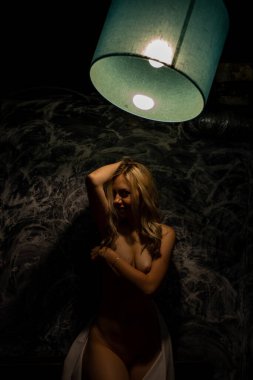 Üstsüz sarışın, siyah arka planda beyaz bir bez ile kaplı.