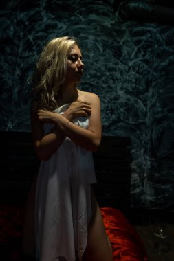 Üstsüz sarışın, siyah arka planda beyaz bir bez ile kaplı.