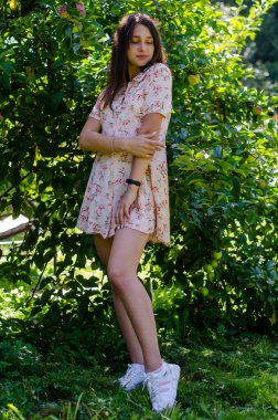 Güneşli bir günde bahçede poz veren yazlık elbiseli güzel bir kız.