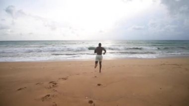 Afrikalı Amerikalı adam sahilde denize doğru koşuyor. şort ve çıplak bluz
