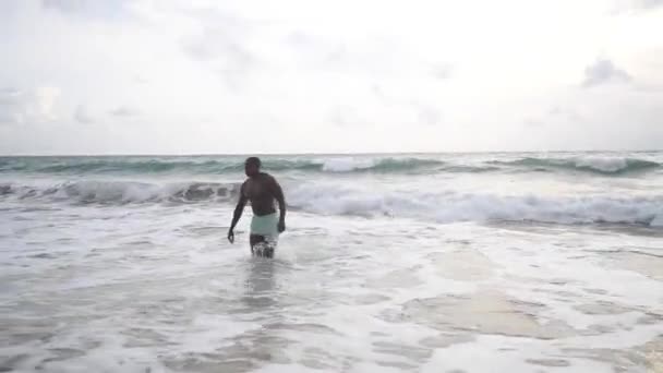 Afroamerykanin biegający po plaży i morzu. spodenki i nagi top — Wideo stockowe