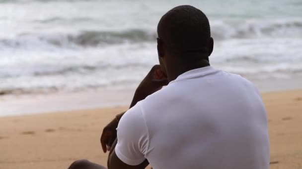 Afro Amerikaanse sportieve man zit op het strand en kijkt naar de zee Stockvideo