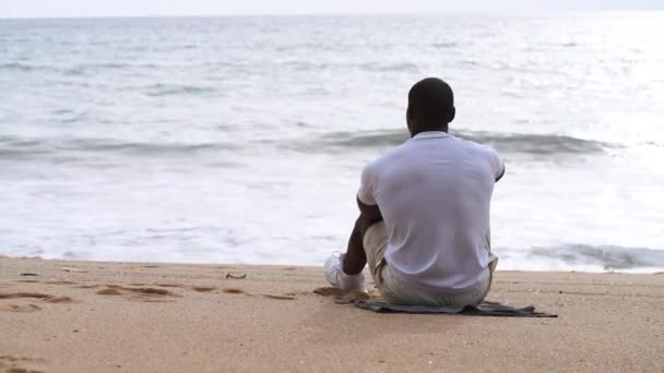 Afro Amerikaanse sportieve man zit op het strand en kijkt naar de zee Stockvideo