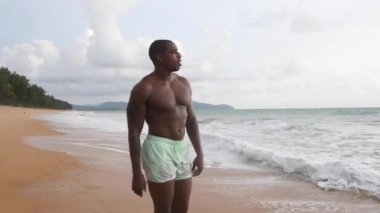 Afrika kökenli Amerikalı adam gün batımında sahilde yürüyor. şort ve çıplak bluz